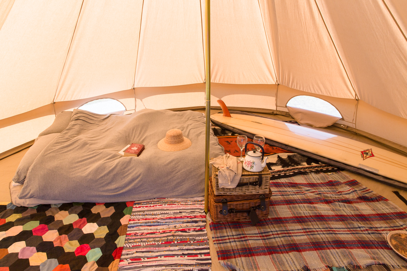 Bell tent interior dressed with rugs, picnic basket, books and surfboard