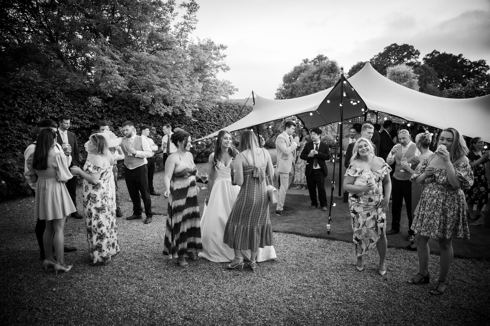 Guests gathered under a stretch tent at dusk in a walled garden