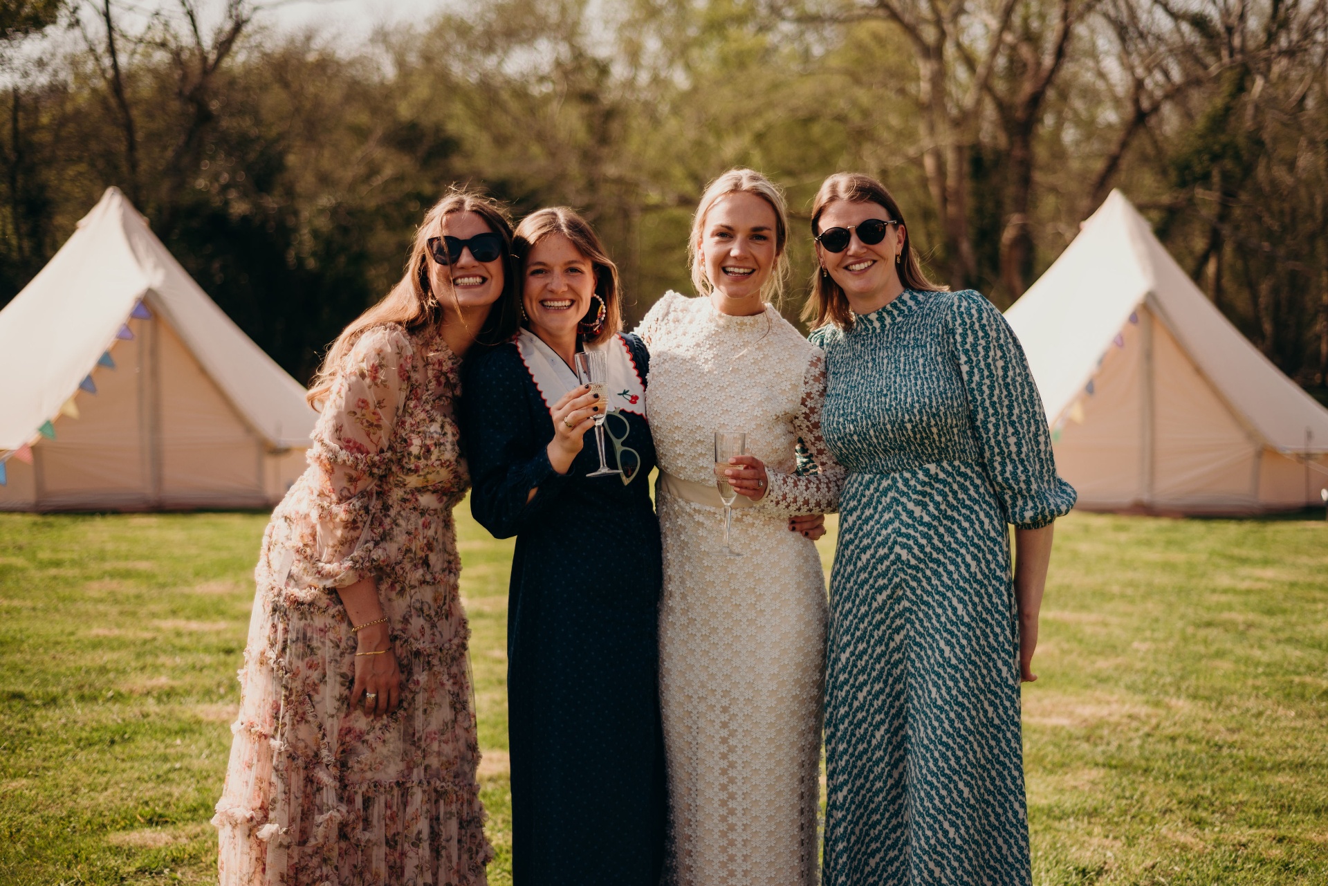 Four wedding guests laughing in front of bell tents