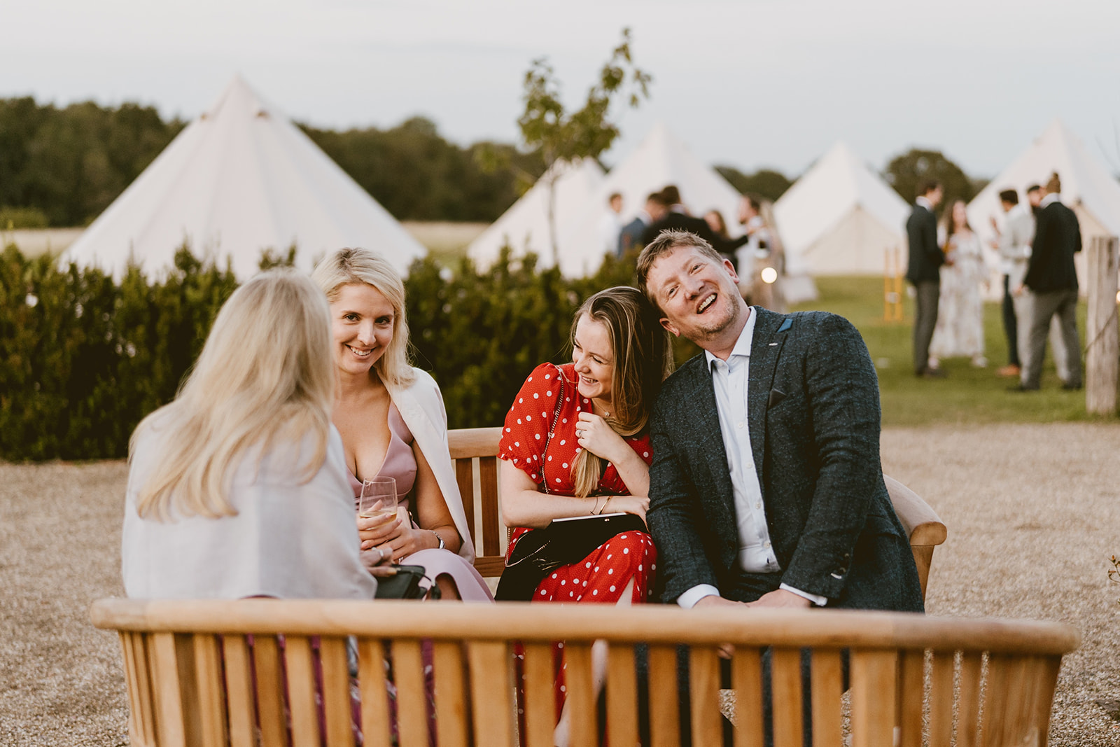 Guests laughing on a bench in front of the bell tent village