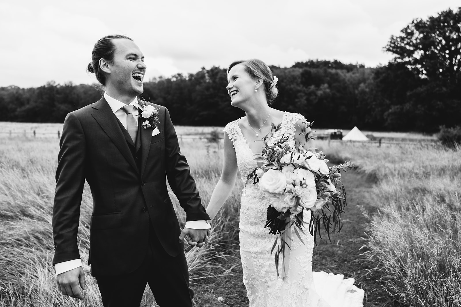 Couple walking in the field with a bell tent behind